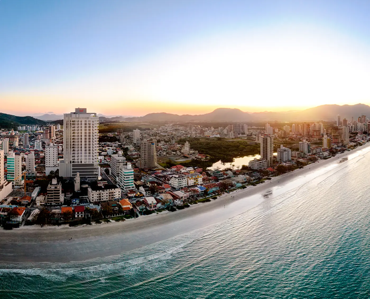 Praia do Balneário Perequê ao pôr do sol, com a orla e os morros de Porto Belo